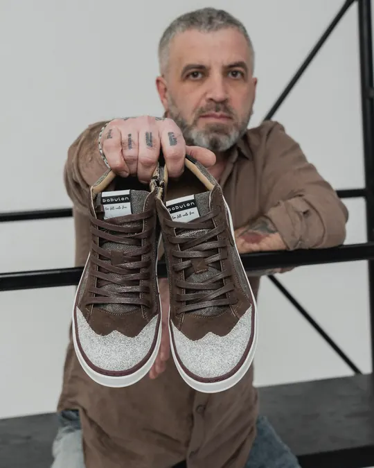 A man holding up a pair of Babylon sneakers