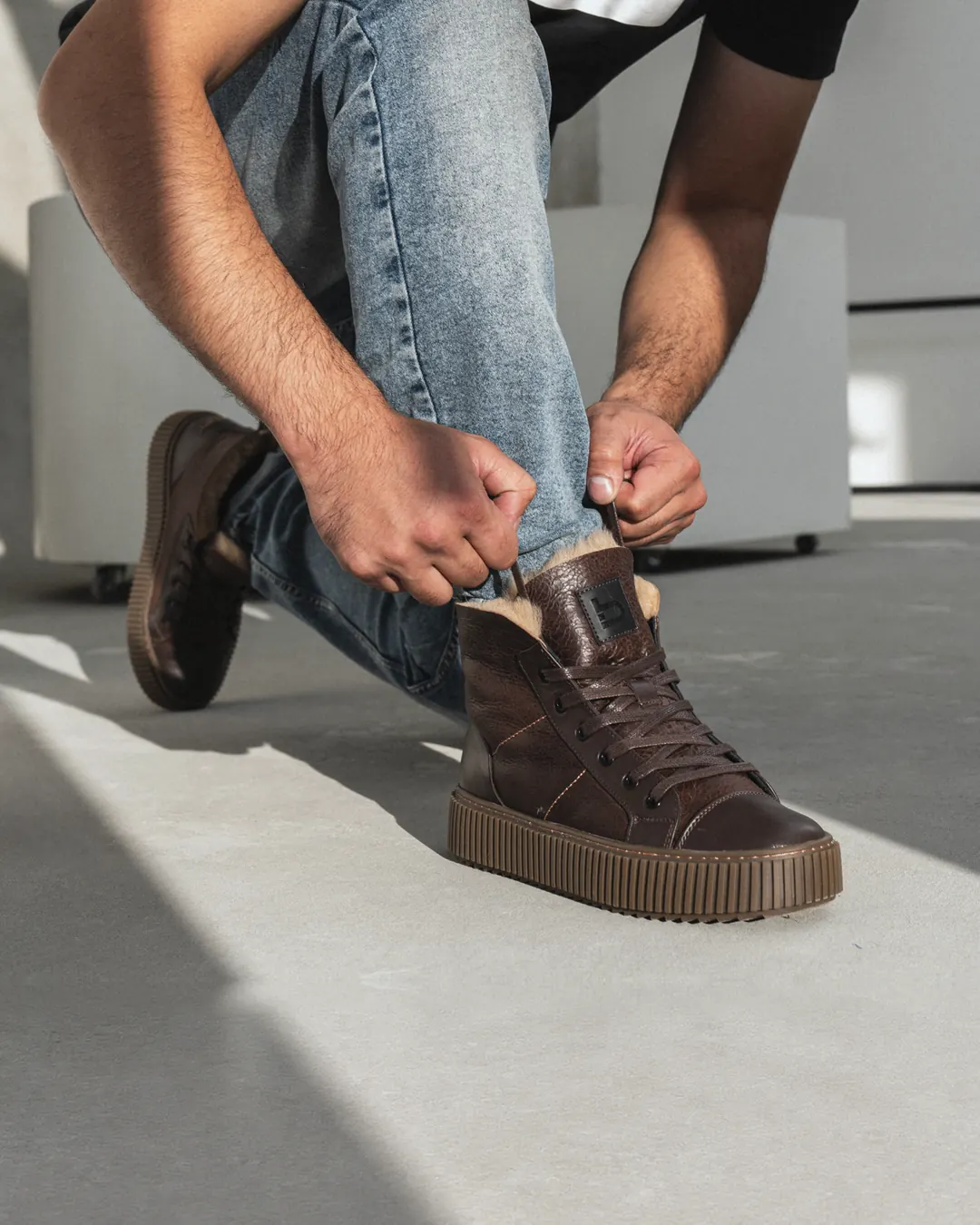 A man in light jeans laces up brown leather Babylon Frost-84 boots lined with sheepskin