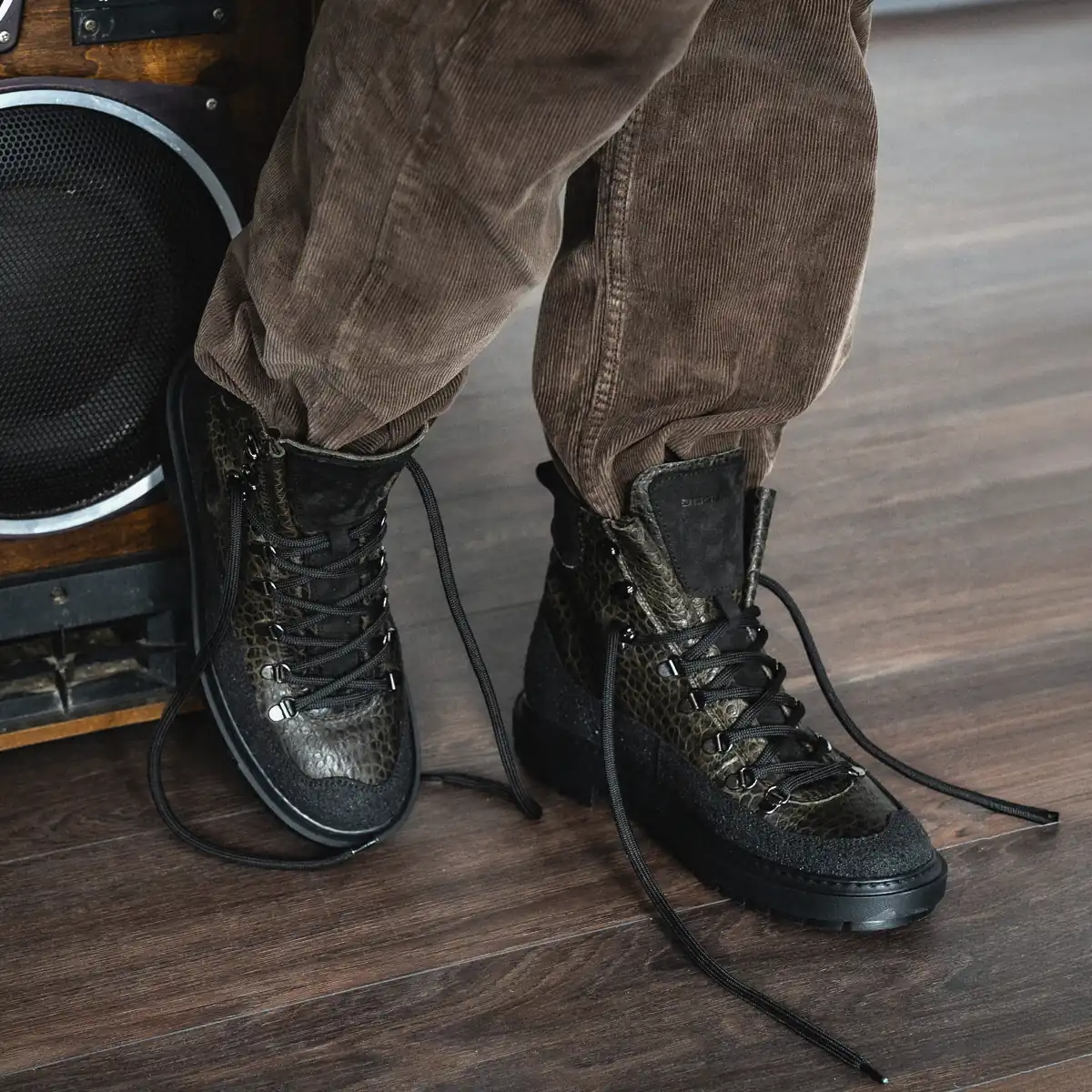 Green leather Babylon Armor-18 boots with loose laces worn with brown corduroy trousers next to a speaker