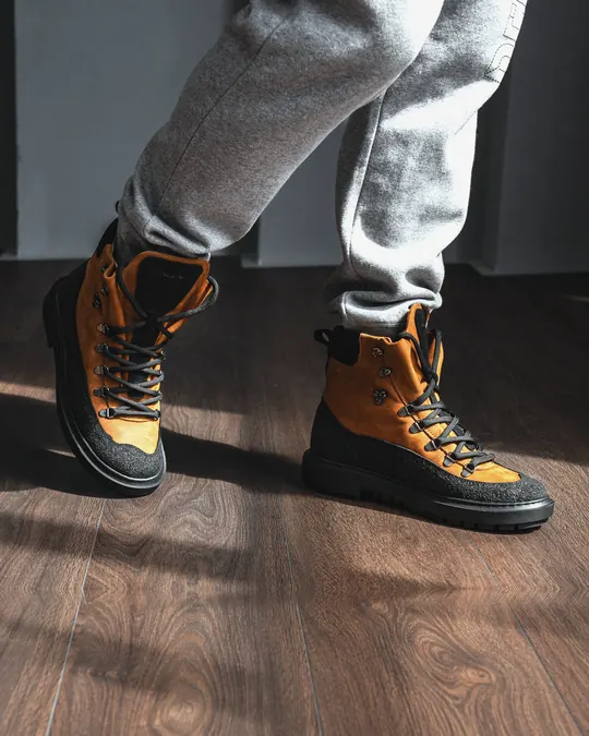 Babylon Armor-24 men's lace-up winter boots in brown and black leather, worn with grey joggers on a wooden floor