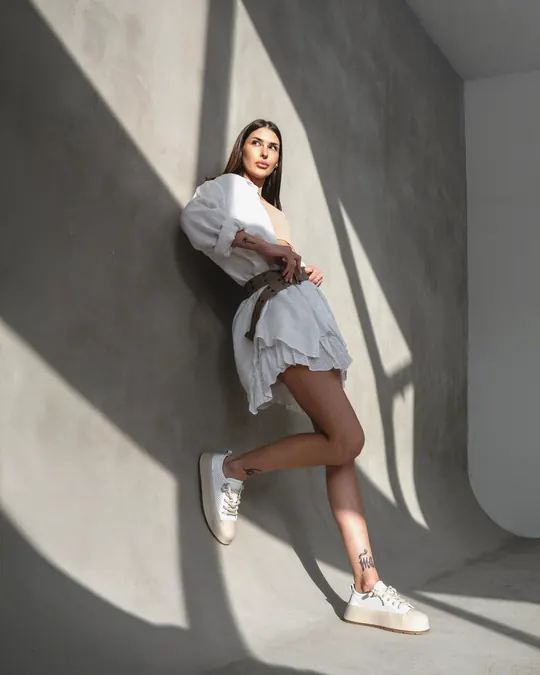 A woman in white Babylon sneakers against a sunlit concrete wall