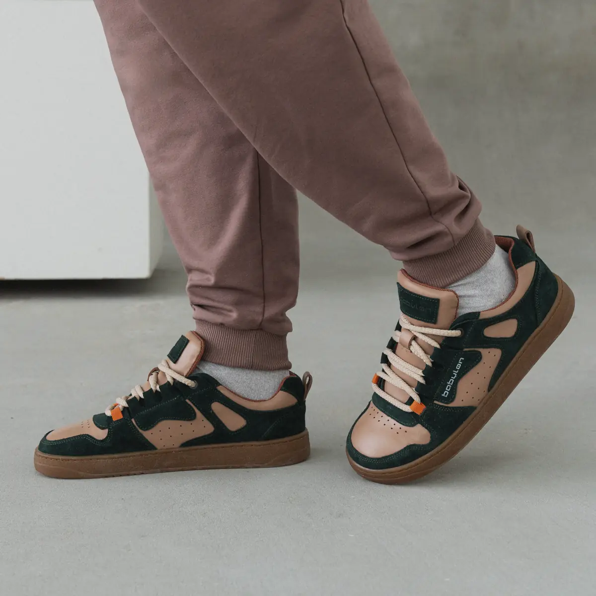 Men's Space-14 sneakers in leather and nubuck, dark green with beige, mid-stride with dusty pink joggers and white socks