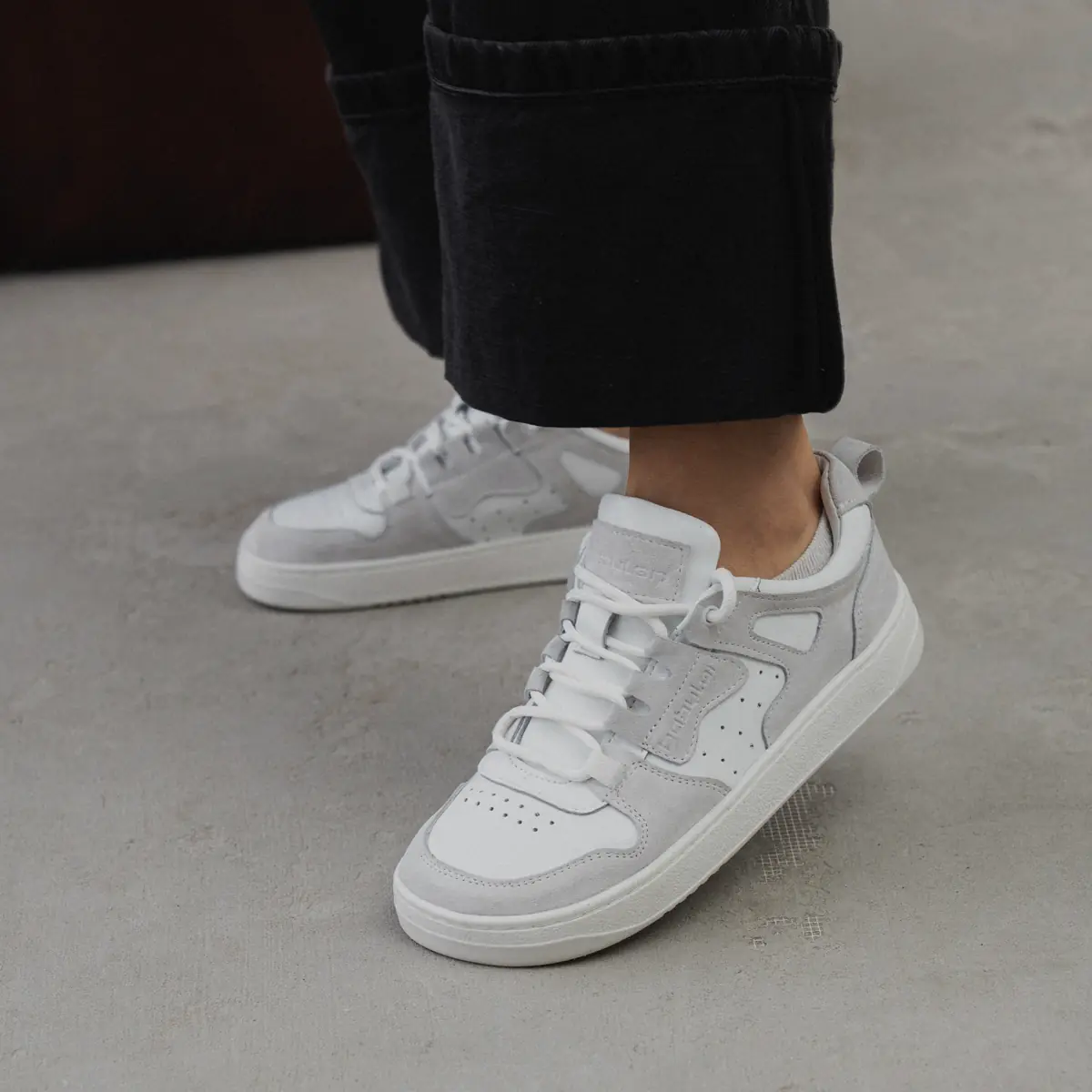 Women's white and light grey Space-90 combination-leather sneakers mid-step on concrete, with wide-cuffed black jeans