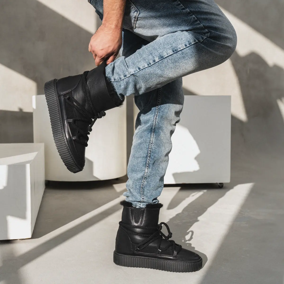 A man in light jeans pulls on black Babylon UGM-1-41 men's lace-up sheepskin boots