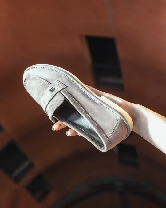 A Babylon suede loafer held in a hand against a terracotta background