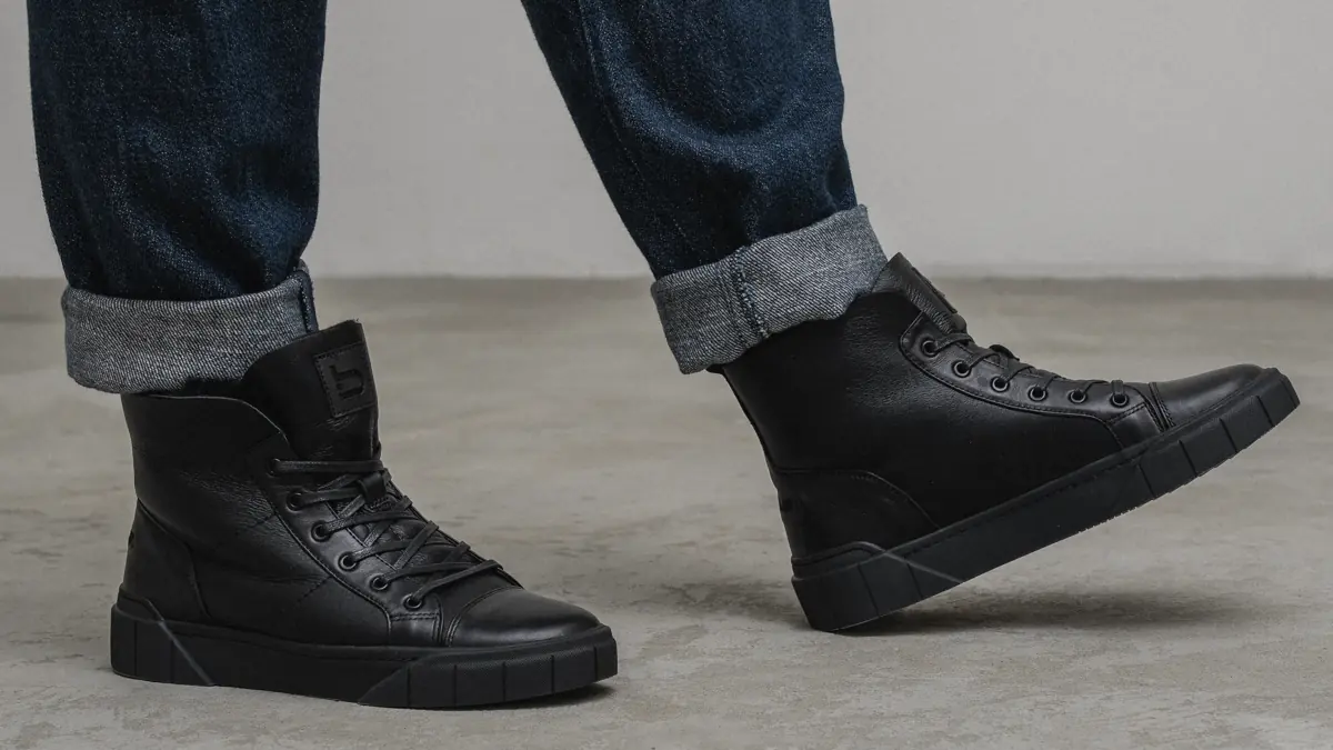 Black leather Frost-11 boots with sheepskin inside, worn by a man in cuffed dark jeans walking on a concrete floor