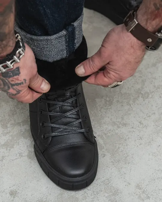 Black leather Frost-11 boots with sheepskin inside, worn by a man in cuffed dark jeans walking on a concrete floor