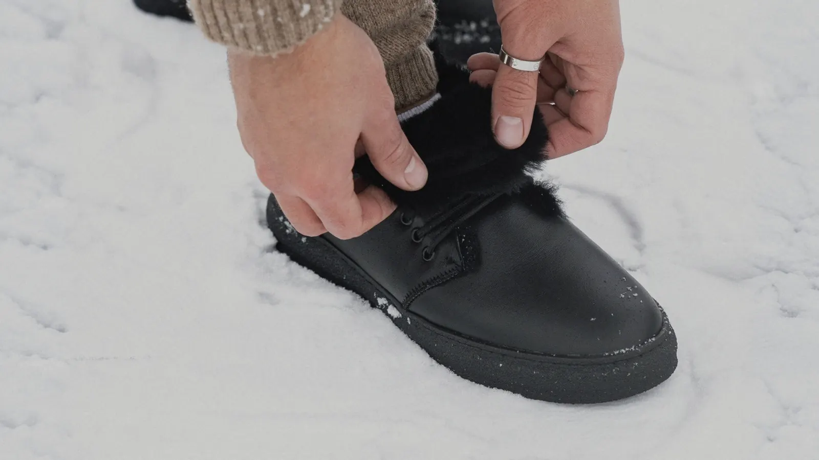 Hands lacing black fur-lined Babylon winter boots in the snow