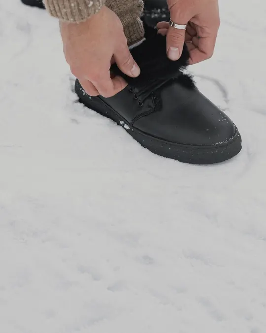 Hands lacing black fur-lined Babylon winter boots in the snow