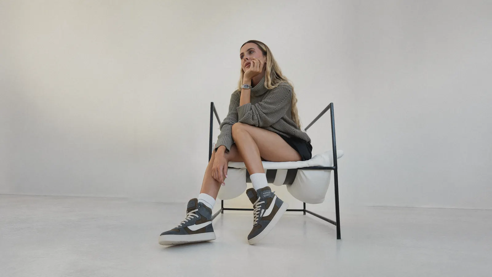 A woman in a chair showing her Babylon high-top sneakers in a bright studio
