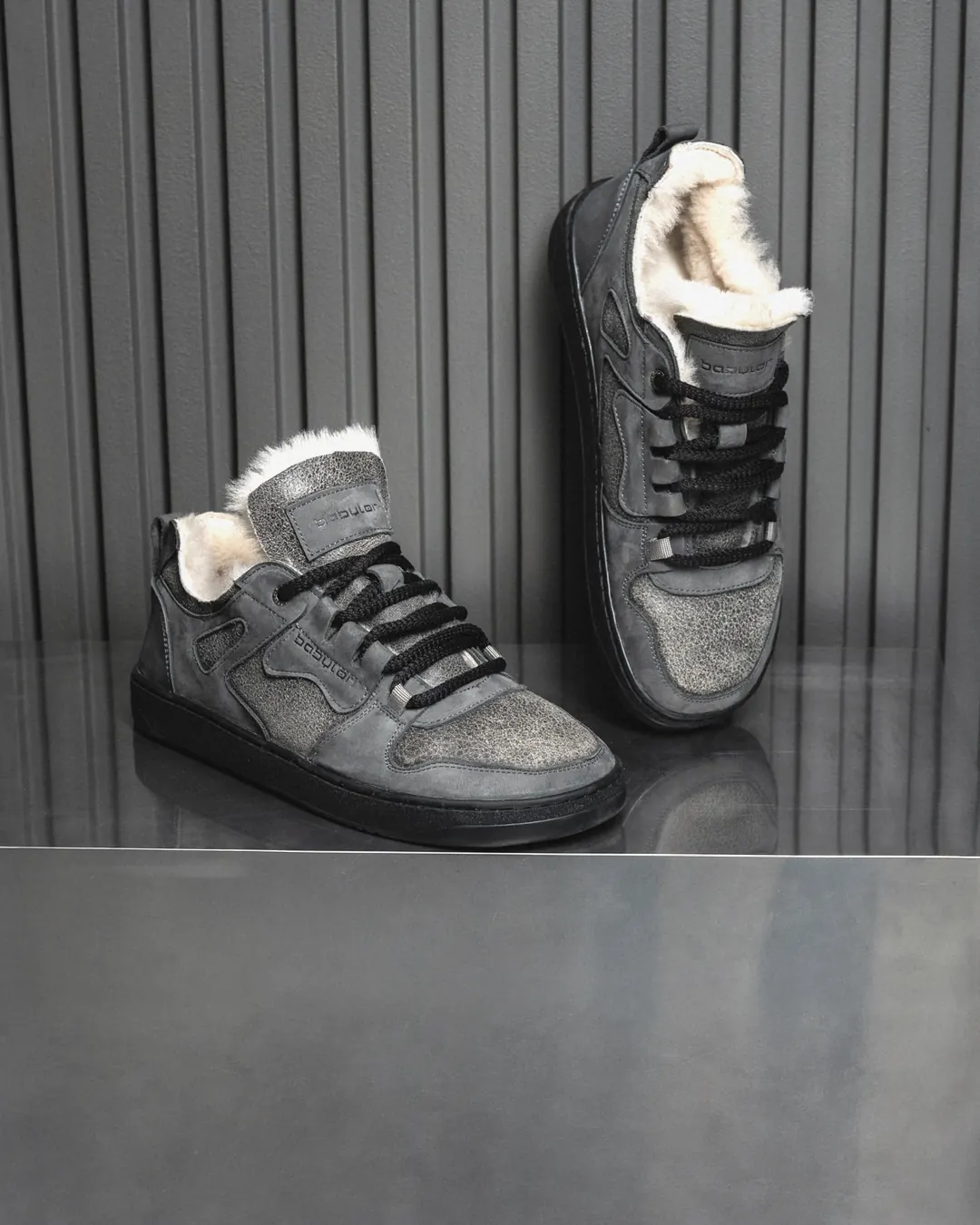 A pair of grey fur-lined Babylon Space-02-D sneakers on a metal shelf against dark panelling